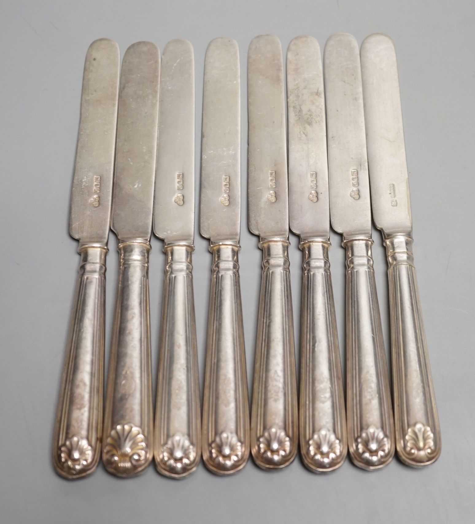 A set of seven Edwardian silver fiddle and shell pattern dessert knives, Goldsmiths & Silversmiths Co Ltd, London, 1909 and a similar plated knife.